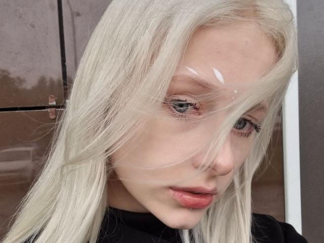 ExcitedBlizzard has platinum blonde hair, blue eyes, and pink lips. A transparent drop is on her forehead. She's wearing a black top, looking slightly down.