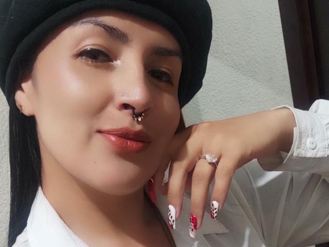 Adafieldd, met een medium bruine huid, draagt een zwarte baret, een wit shirt en rode lippenstift. Ze heeft een neusring, een ring met een diamant en verzorgde nagels met rode en witte patronen..
