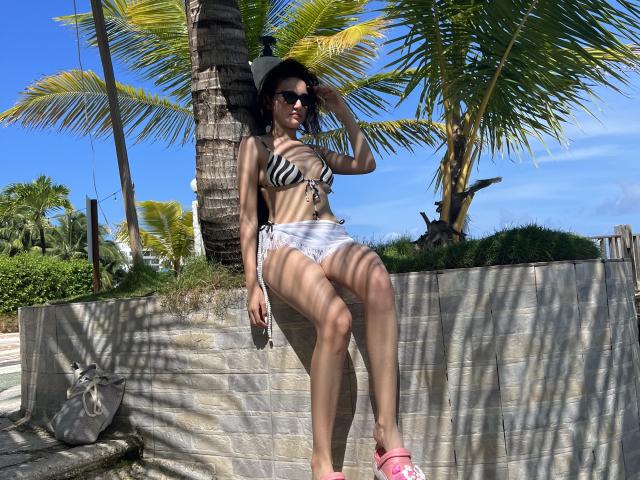 EstefaniaRamosHot com top de biquíni listrado, shorts brancos, sandálias rosa, chapéu de sol, óculos de sol, sentada no concreto, palmeiras, padrão de sombra, segurando o celular, pele bronzeada, seios médios, sexy, tropical..
