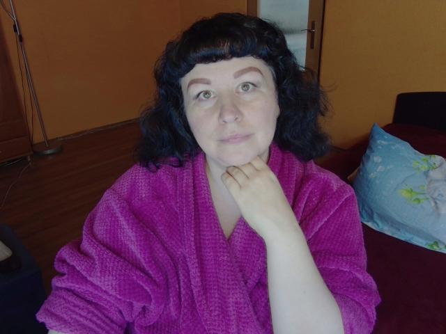 ErinSmart, con cabello negro y rizado, vestida con una bata rosa y esponjosa, tiene un tono de piel claro y está apoyando su barbilla en la mano, mirando directamente a la cámara..