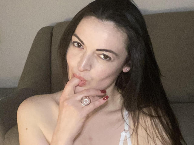 JulliGlei, con cabello largo y oscuro, piel clara y uñas rojas, se chupa el dedo con un anillo en la mano, mirando a la cámara con una ligera sonrisa..