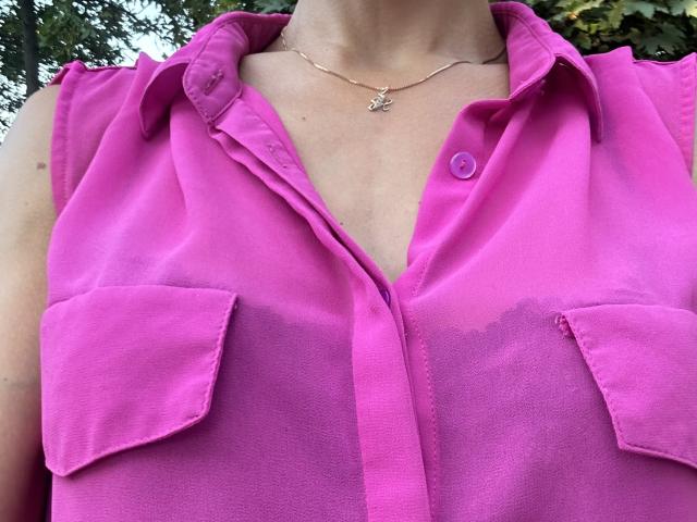 BellaJulls portant une chemise rose à boutons, laissant entrevoir ses seins à travers le tissu, boutonnée jusqu'en bas, avec des poches sur la poitrine, un collier en argent avec une petite étoile, à l'extérieur..