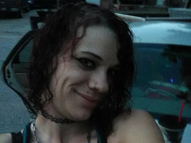 FreakySaint mit nassen, lockigen braunen Haaren, Nasenring, schwarzem Choker und einem leichten Lächeln, die ihre Brüste zeigt, sieht in einem schwach beleuchteten Auto sexy aus..
