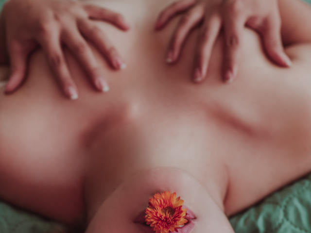 SallyDoll's bare back with hands on her tits, a flower over her pussy, soft pink skin, gentle lighting, fingers spread, nails clean, subtle eroticism, intimate close-up.
