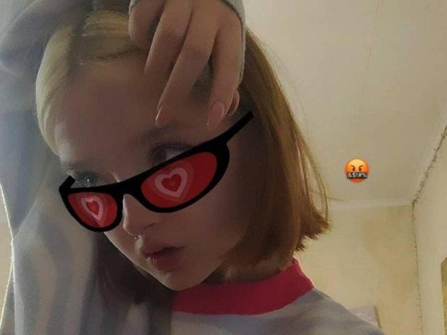 LaPochka, avec ses yeux en forme de cœur rouges, ses lunettes noires et son air boudeur, portant une chemise rayée, a une main dans ses cheveux, et un petit emoji en haut à droite..