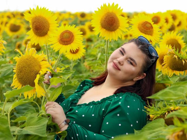 KaidoKun, avec un visage illuminé par le soleil, portant une robe verte à pois, tenant des tournesols, des lunettes de soleil bleues sur la tête, souriant, entouré d'un champ de tournesols, et ayant une allure adorable..
