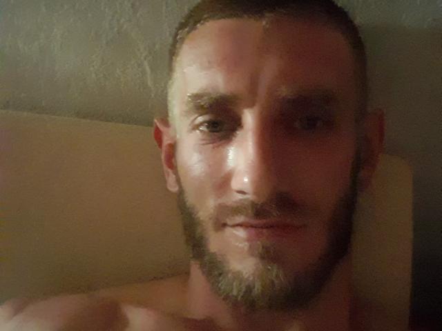 HoroXsun, um homem sem camisa, com barba, cabelo curto e um leve sorriso, tem um rosto levemente suado, com um nariz pequeno e olhos castanhos..