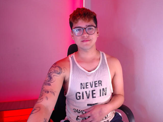 EddTerence, um jovem corpulento de óculos, vestindo uma camiseta branca e mostrando um braço tatuado, sentado em uma cadeira com iluminação rosa..