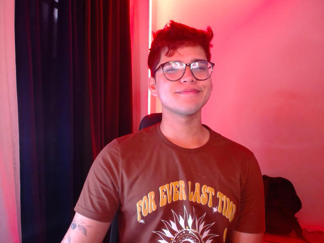 EddTerence with short, curly brown hair, glasses, and a brown shirt with "For Every Last Day" has a small tattoo on his right arm and a slight smile.