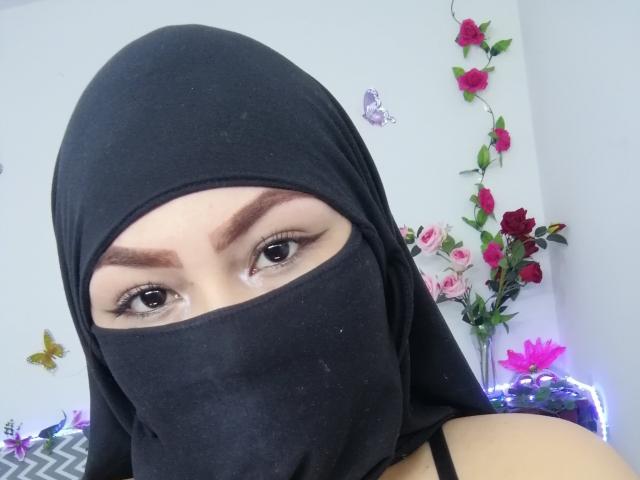 ElinaX, con un hijab nero che le copre il viso, mostra sopracciglia castane, occhi scuri con eyeliner e un naso visibile. Le sue spalle nude sono visibili..