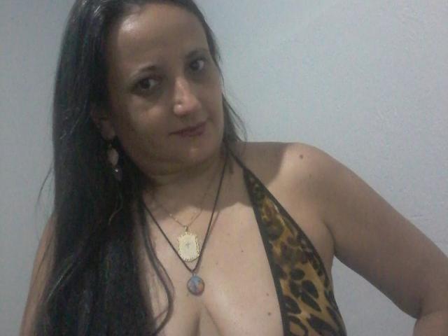 SheronShiedss, con lunghi capelli scuri, indossa un top a fascia leopardato che mette in mostra il seno, una collana con un ciondolo rotondo e un sorriso appena accennato..