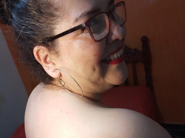 Loretta Sanchez, mit rotem Lippenstift, Brille und Reifenohrringen, lächelt in die Kamera, wobei ihr nacktes Schulter und ein kleines Ohrpiercing zu sehen sind. Ihr braunes Haar ist zu einem unordentlichen Dutt gebunden..