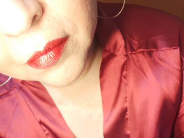 Loretta Sanchez' Gesicht mit glänzendem rotem Lippenstift, leicht geöffneten, glänzenden Lippen und einem seidigen, rosa Hemd, das vom Kinn abwärts sichtbar ist, mit großen Reifenohrringen..