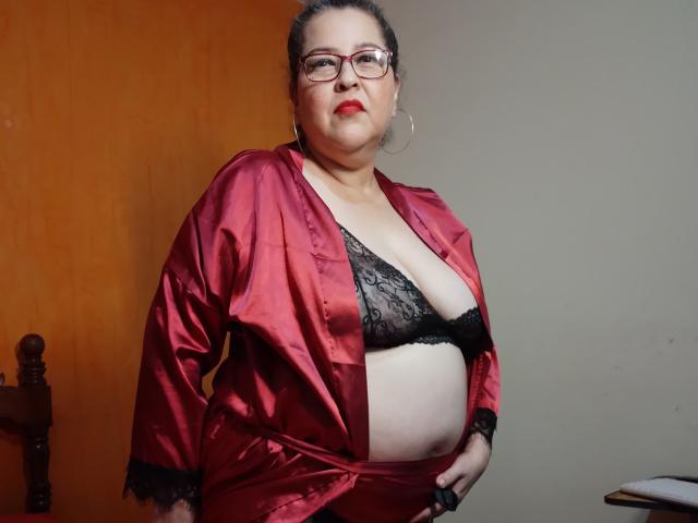 LorettaSanchez, plus-sized with red lipstick, wearing a red satin robe open to reveal black lace bra, showing her big tits and belly, standing with hands on hips.