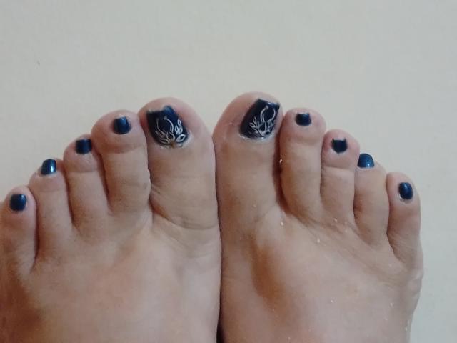 Les pieds de Loretta Sanchez, avec du vernis à ongles noir, une orteil ornée d'un motif de feuille blanche, sur un fond uni. Ses orteils sont légèrement humides..