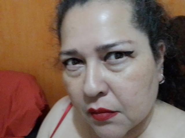 Loretta Sanchez ha il rossetto rosso, l'eyeliner nero e i capelli ricci e scuri, con un'espressione seria, indossa una maglietta rossa e piccoli orecchini. La sua pelle è chiara con un leggero riflesso..