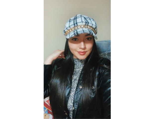 Antonnella Tyler, com cabelos longos e pretos, usando um gorro xadrez, jaqueta de couro preta e uma camisa com estampa de zebra, sorrindo levemente, parecendo adorável com uma maquiagem discreta..