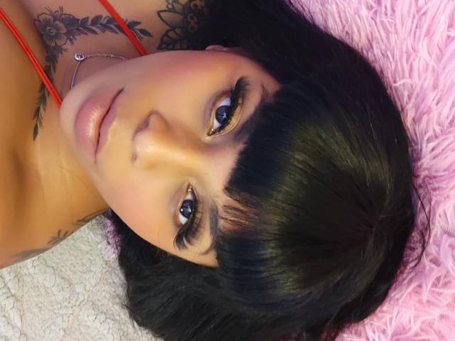 Chili met kort zwart haar en blauwe ogen, liggend op een roze pluizig oppervlak, het dragen van een rode ketting, op zoek.