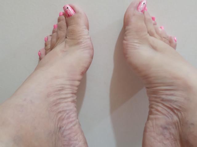 Os pés de Loretta Sanchez, com esmalte rosa nas unhas dos dedos, mostrando solas enrugadas e pele levemente suja, posicionados com os dedos apontando para cima, visíveis de baixo..