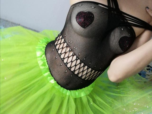 HarlyMia's black fishnet top with heart-shaped black sparkly pasties covering her tits, over a bright green, fluffy, tulle skirt. HarlyMia's arm is visible, holding the top.