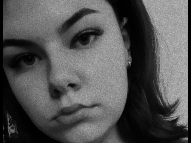 Selfie en blanco y negro de TinaMoore con cejas pobladas, nariz pequeña, labios ligeramente fruncidos y pequeños aretes, mostrando una expresión seria. El cabello oscuro de TinaMoore está a la derecha..