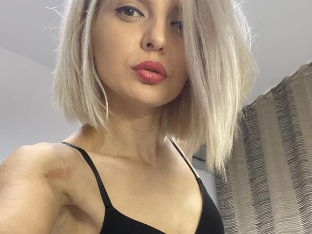 DouceAmelia with blonde bob, red lipstick, black bra, slight bruise on left shoulder, looking at camera, light skin, medium build, slightly parted lips, soft light.