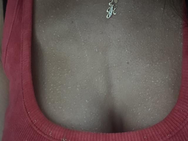 BellaJulls' boobs in a red tank top, showing a bit of cleavage with a silver necklace resting on her chest. Skin texture is visible.