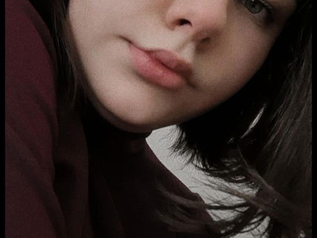 TinaMoore's face with light skin, brown eyes, and slightly pouty pink lips. She's wearing a dark red shirt, and her brown hair is partially visible on the right.