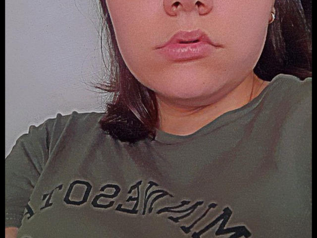 O rosto de TinaMoore, com lábios rosados levemente curvados, cabelo castanho na altura dos ombros e uma camisa verde que mostra seus pequenos seios. Ela está usando um simples brinco de ouro..