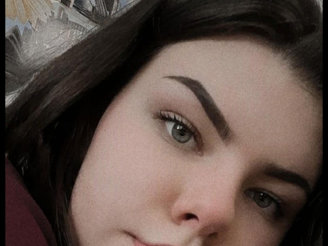 Il viso di TinaMoore, che mostra i suoi occhi verdi, le sopracciglia scure e le labbra leggermente dischiuse con un accenno di sorriso. I suoi capelli castano scuro sono parzialmente visibili a sinistra..