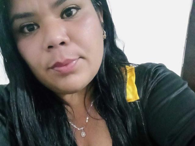 LiAngel has shiny black hair, a cute face with pink lips, and wears a black shirt with a yellow strap. She's looking at the camera with a slight smile.