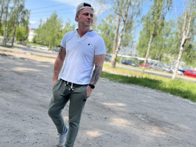 MichaelHero, camicia polo bianca, pantaloni verdi, mani in tasca, berretto da baseball, tatuaggio sul braccio destro, orologio da polso, cammina su ghiaia, cielo blu, alberi verdi, casual, sicuro di sé, attraente..