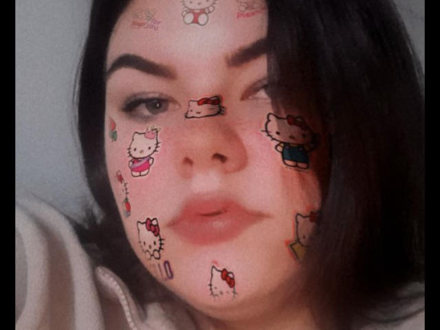 El rostro de Tina Moore está cubierto de tatuajes de Hello Kitty, con adorables diseños de dibujos animados en su frente, mejillas y nariz. Ella está guiñando un ojo, con cabello castaño oscuro, y tiene una expresión ligeramente seria..