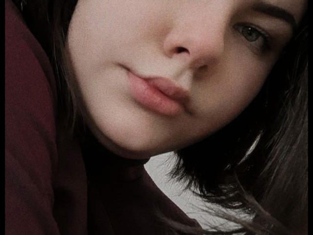 Das Gesicht von Tina Moore auf einem Selfie, das ihre helle Haut, ihre dunkelbraunen Augen und ihre leicht geöffneten, rosafarbenen Lippen zeigt, wobei ihr dunkelbraunes Haar ihr rechtes Auge teilweise bedeckt..