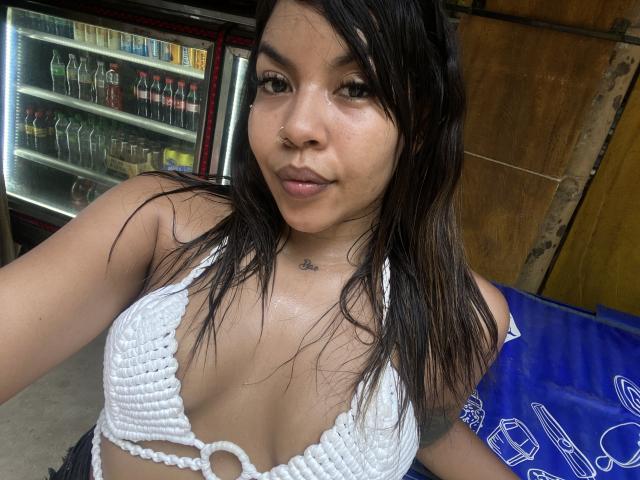 ValerySquirting with wet black hair, small nose ring, white crochet bikini top, showing her tits, small tattoo under chin, smiling at camera, standing in front of fridge.