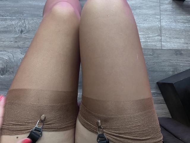 ArleenHunter's legs in sheer brown thigh-highs, showing her knees and upper thighs, with black straps on the garter tops, on a wooden floor.