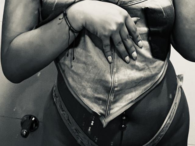 ShantalSummer's hand rests on her chest, wearing a zip-up, sleeveless top, with a black bracelet, and lace-trimmed underwear, showing a belly button with two silver studs.
