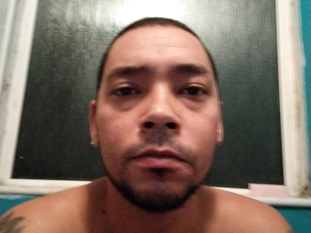 RocioHotMan has a shaved head, small goatee, and is shirtless with a neutral expression. His face is centered, with a dark, textured background behind him.