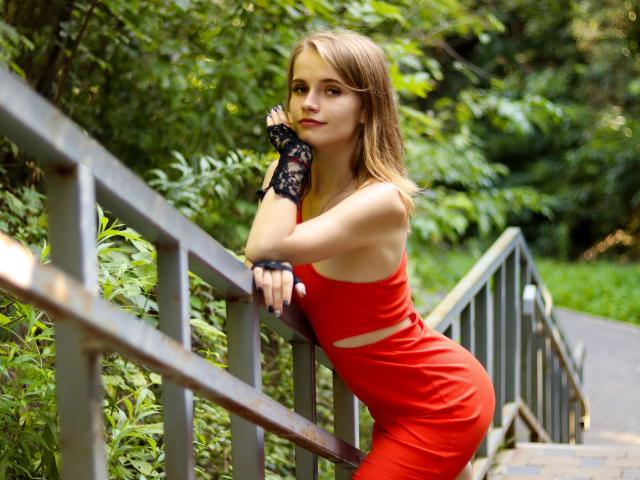 MargaritaKis in a red dress, black lace glove, leaning on a metal railing, green leafy background, brown hair, cute face, small tits, slim, sexy, confident, outdoor setting.