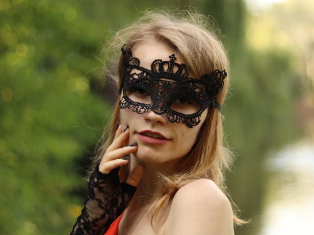 MargaritaKis met een zwart kanten masker, dat haar lippen aanraakt, draagt een rode top, blond haar en een zwarte kanten handschoen, en laat haar borsten zien. Groene achtergrond..