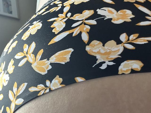 BlueMaryAnnes schwarze Unterhose mit gelben und weißen Blumenmustern, die ihr kurviges Hinterteil zeigen. Der Stoff ist leicht strukturiert, und die gelben Blumen sind deutlich sichtbar..