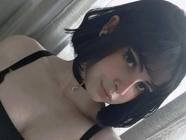GothOfAngie ha i capelli neri tagliati corti, la pelle chiara e piccoli seni, indossa un choker nero e un vestito a spalline, con un sorriso appena accennato, mentre guarda nella fotocamera..