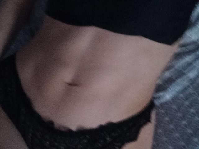 DanceErika's bare midriff with a small navel, wearing black lace panties, slightly blurred, with a dark bra top. Soft, dim lighting.
