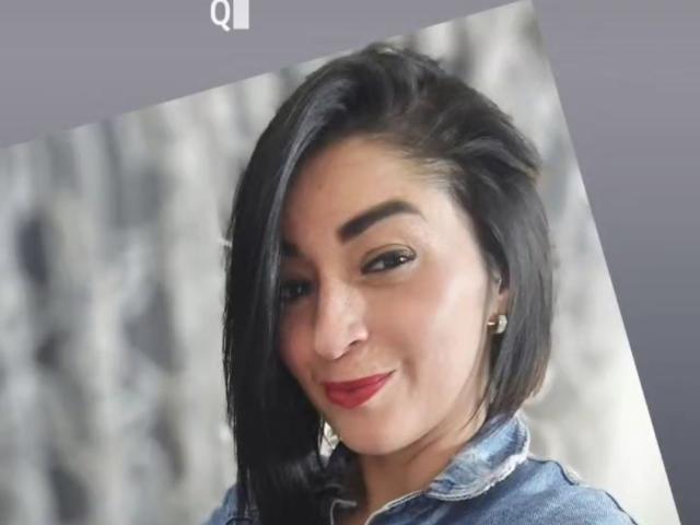 KarenBroc tiene el cabello negro de longitud media, lápiz labial rojo y está sonriendo ligeramente, vistiendo una chaqueta vaquera. Lleva aretes pequeños y tiene la piel de color marrón claro..