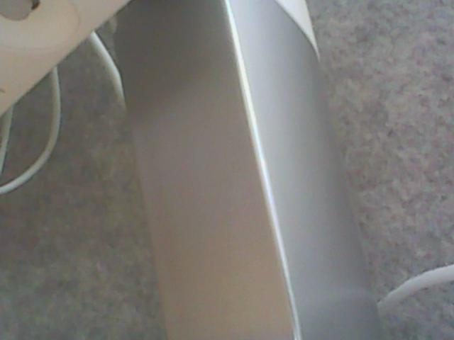 Tubo metallico a forma di boogie, con una superficie lucida e liscia, posizionato diagonalmente nell'immagine. Sullo sfondo si trovano un cavo bianco e un tappeto grigio..