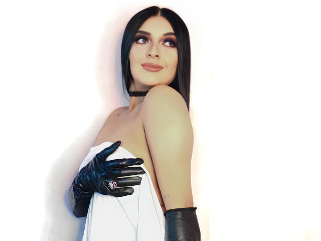 ArianaCortes with black gloves, white dress, and choker, holding a white cloth over her tits, looking up with a subtle smile, long black hair, white background.