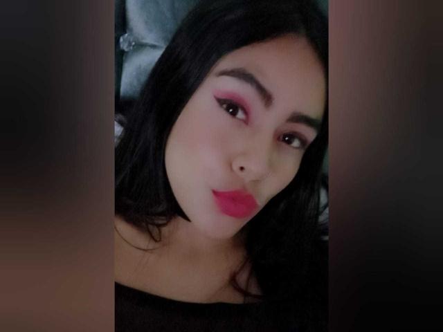 StellaBeckker with dark hair, pink eyeshadow, black eyebrows, red lipstick, and a slight smile, looking up with a soft, cute expression. Her tits are not visible.