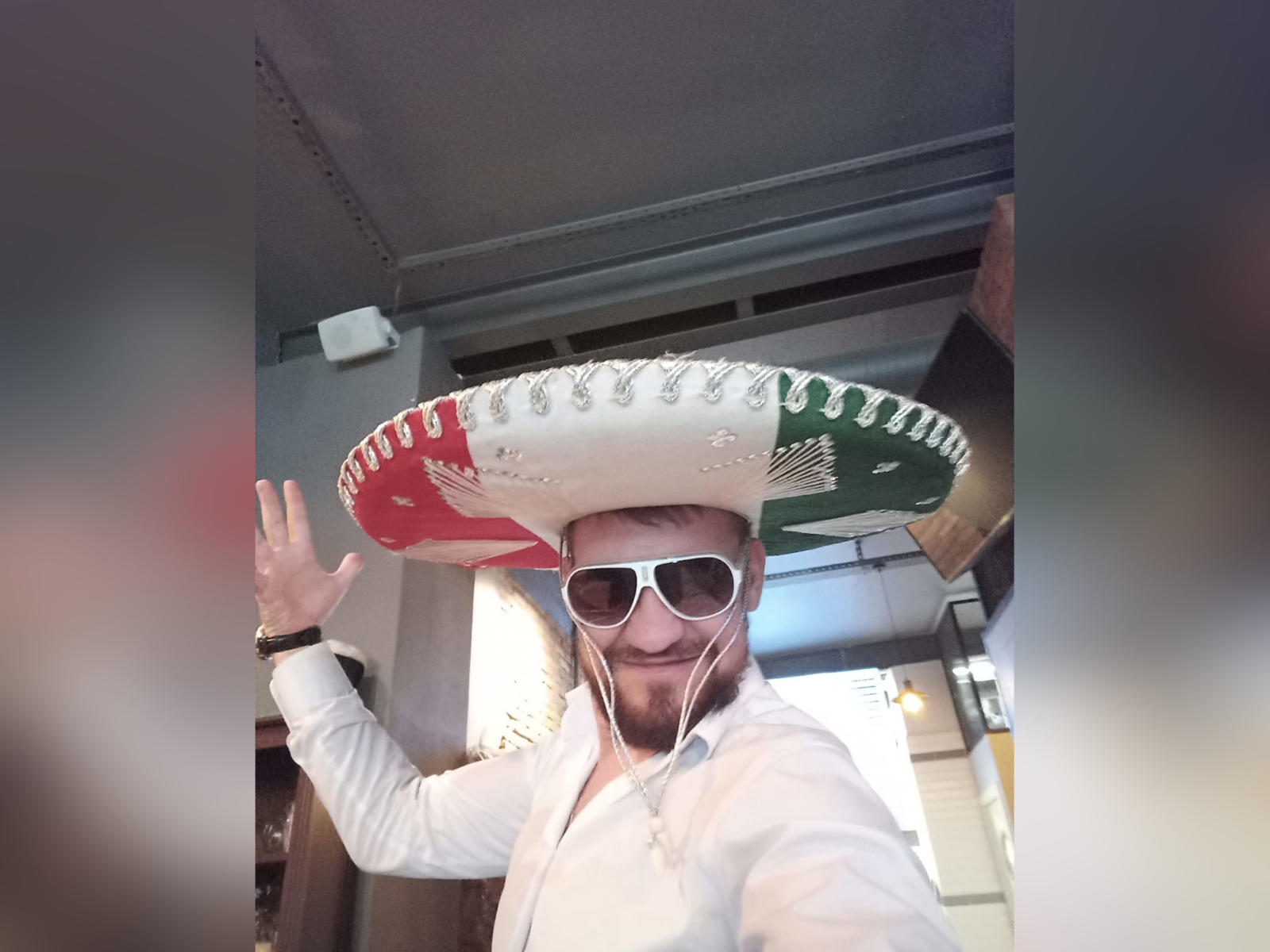 PasitiF trägt einen riesigen mexikanischen Sombrero, weiße Sonnenbrillen und ein weißes Hemd, winkt lächelnd, hat einen Bart und trägt weiße Kopfhörer..