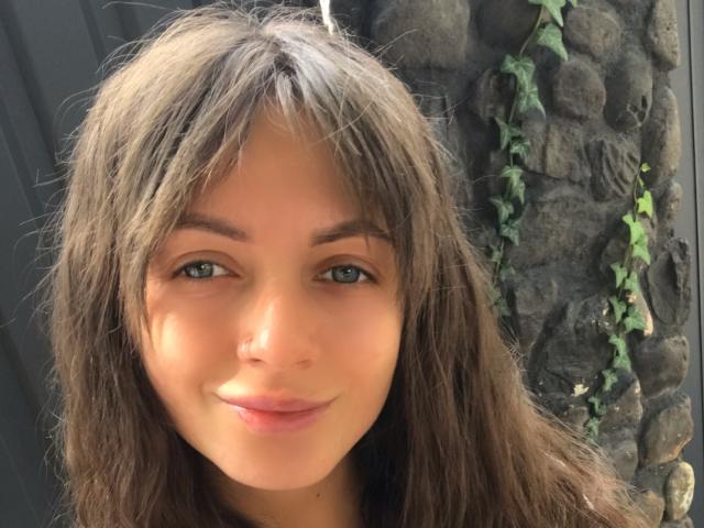 LikaLuis a de longs cheveux bruns, des yeux bleus et un petit nez avec un sourire discret. Ses seins ne sont pas visibles. Elle se tient près d'un mur de rochers recouvert de lierre..