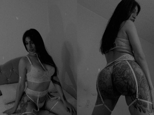 Black-and-white photo of BellaMariee with long dark hair, lace bra, garter belt, and tattoos, showing her tits and ass, standing and kneeling, looking down and back.